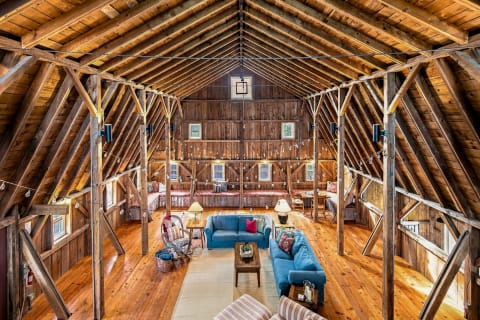 A spacious living area inside a beautifully converted barn, featuring wooden beams, sofas, and decorative lighting.