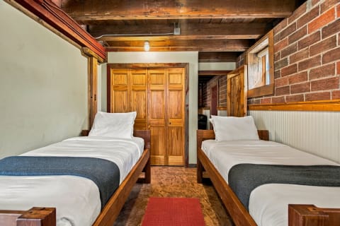 Interior view of a cozy room featuring two twin beds, rustic wood beams, and brick walls.