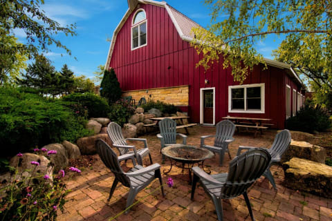 A red barn-style property with a landscaped patio and fire pit seating under trees.