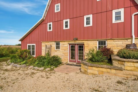 A red barn-style property with stone base, double glass doors, and lush greenery.