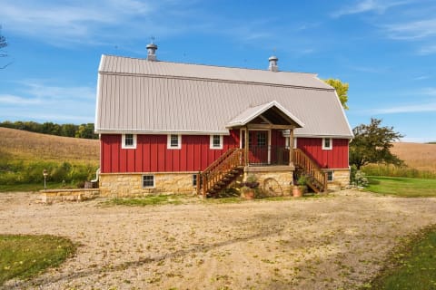 A red barn-style house with a stone foundation in a rural setting under a clear blue sky.