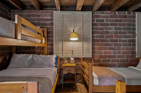 A cozy sleeping quarters with wooden bunk beds, a nightstand, and exposed brick walls.