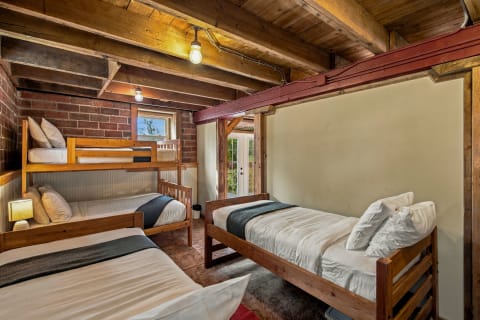 Cozy sleeping space featuring wooden bunk beds and single beds against a backdrop of exposed brick and wooden beams.