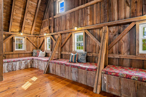 Interior of a barn retreat with wooden beams, built-in seating with vintage cushions, and natural light through windows.
