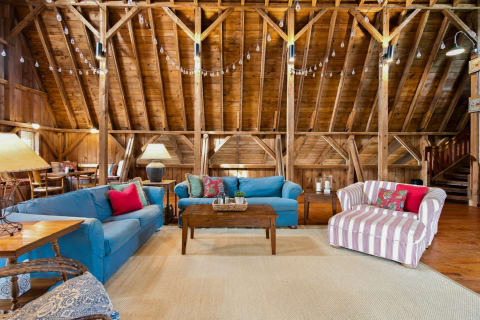 Cozy barn-style living area with blue sofas, a striped armchair, and wooden beams accentuating the rustic charm.