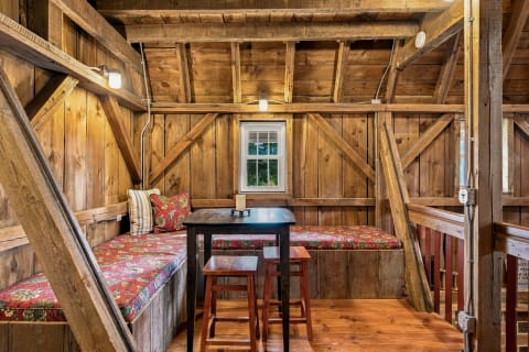 A rustic dining nook with wooden beams, floral cushioned bench, and dark wood table.