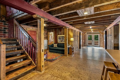 A rustic entryway featuring wooden beams, brick walls, a green couch, and a staircase leading to an upper level.