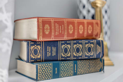 Three stacked classic literature books with ornate bindings resting on a white shelf.