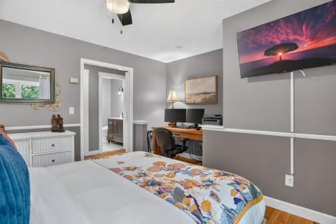 A peaceful bedroom with a comfortable bed, dual monitors for work, and artistic decor.