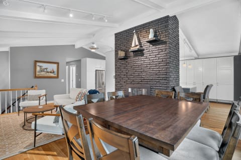 A spacious dining area with a wooden table and a brick fireplace, complemented by vaulted ceilings and natural light.