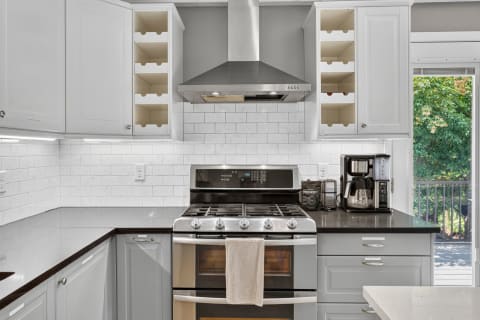 Bright and contemporary kitchen with a gas stove, gray and brown countertops, and a view of greenery outside.