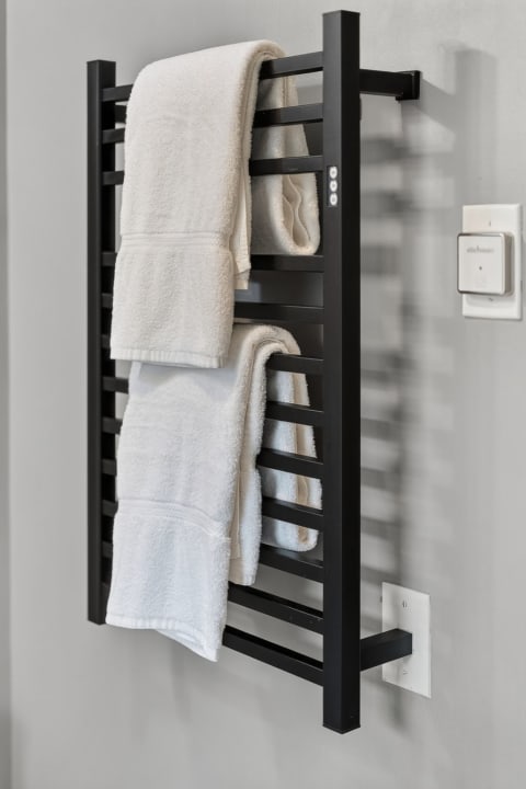 A black towel warmer mounted on a gray wall with two white towels draped over it.