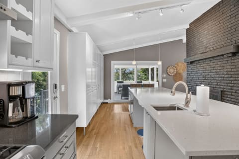 Bright and modern kitchen with white cabinets, hardwood floors, and a brick accent wall, featuring a large island and outdoor view.