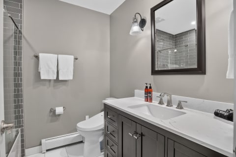 Modern bathroom with gray walls, white towels, dark wood vanity, and a glass-tiled shower.