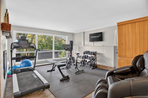 Private fitness room with treadmill, stationary bike, weights, exercise ball, and large windows.
