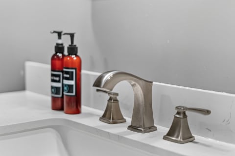 Close-up of a brushed-nickel faucet beside two amber bottles in a modern bathroom setting.