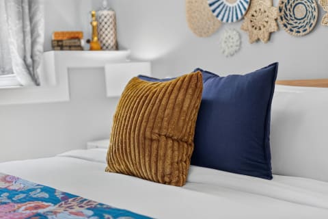 Two textured pillows in mustard and navy rest on a white bedspread in a serene bedroom setting with floral accents.