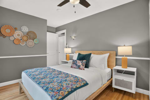 Cozy bedroom with a queen bed, colorful quilt, artistic wall decor, and warm lighting.