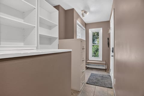 Bright entryway featuring white shelves, a beige filing cabinet, and a sunny view of trees through the window.