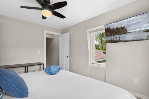 Cozy bedroom featuring a bed, a TV, and a window with green foliage outside.