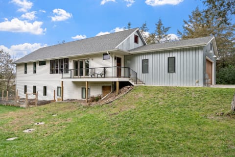 Modern house with a blend of white siding and gray metal exterior, set on a grassy slope.