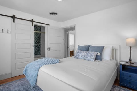 A serene bedroom with a white bed, blue throw blanket, and a bedside lamp, showcasing minimal coastal decor.