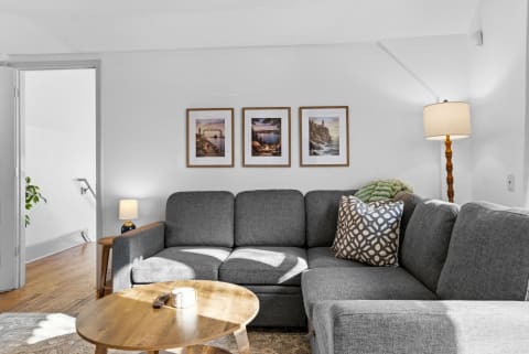 Cozy living room with gray sectional sofa, wooden table, and framed prints.