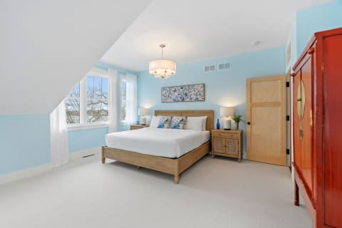 A bright and stylish bedroom featuring a white bed with blue pillows, soft blue walls, and a red armoire.