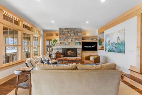 Cozy living room with stone fireplace, plush sofa, and large windows.