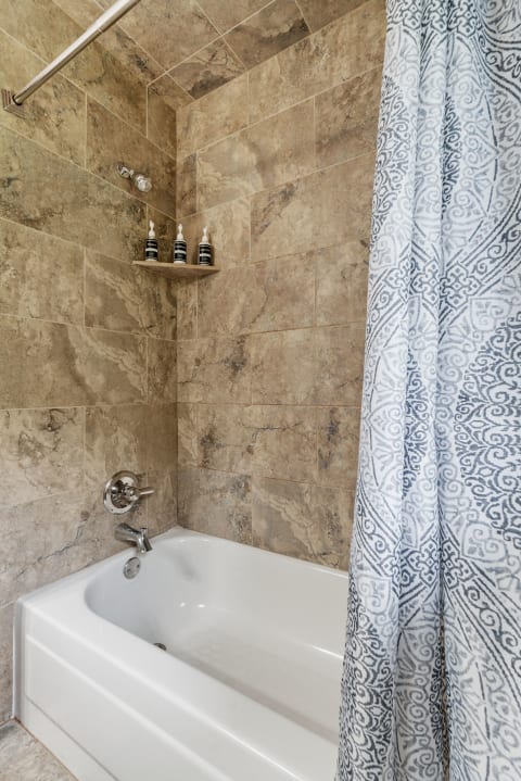 Modern bathroom with beige stone tiles and a bathtub.