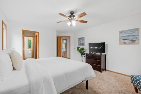 An inviting bedroom featuring a bed, dresser with TV, and bright decor.