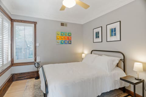 A modern bedroom with a white bed, colorful artwork on the walls, and wooden accents.