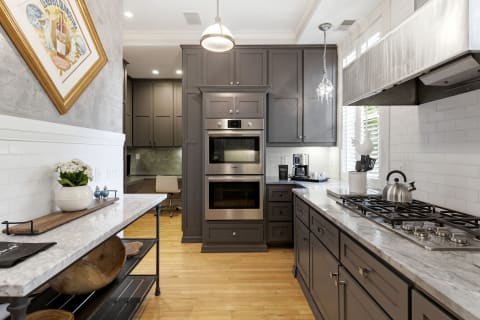 A sleek modern kitchen featuring gray cabinets, marble countertops, and stainless steel appliances.
