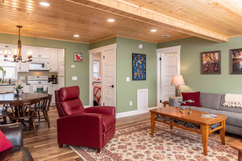 A cozy living room with a red recliner, gray sofa, and a wooden dining table in a well-lit interior.