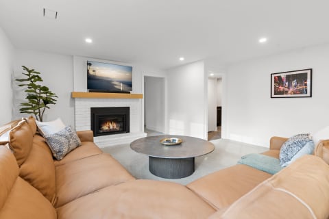 A contemporary living room with a leather couch, fireplace, and a television displaying a sunset over the beach.