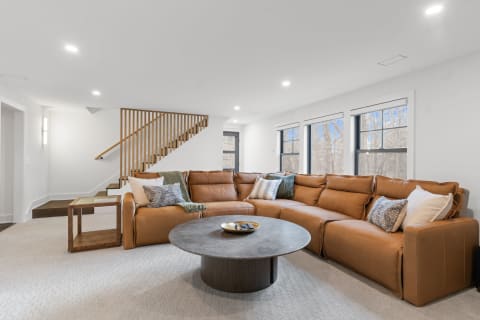 A spacious living room featuring a brown leather sectional sofa, a round coffee table, and large windows with a view of nature.