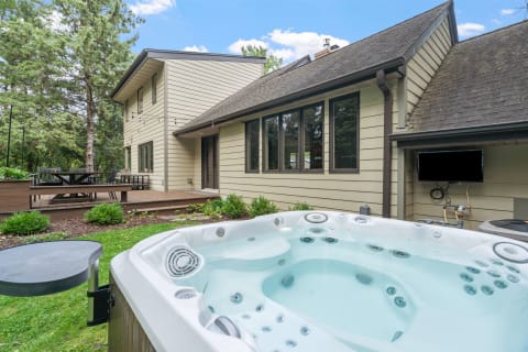 Backyard scene with a hot tub and wooden deck surrounded by trees.