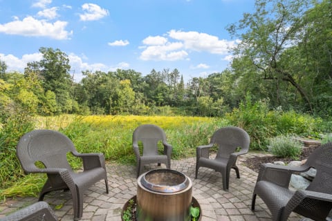 Fire pit area with chairs and a view of greenery and blue sky.