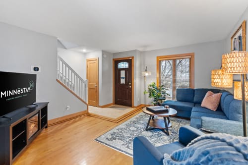 Settle into your stylish living room with plush blue seating, warm hardwood floors, and natural light streaming through large windows.