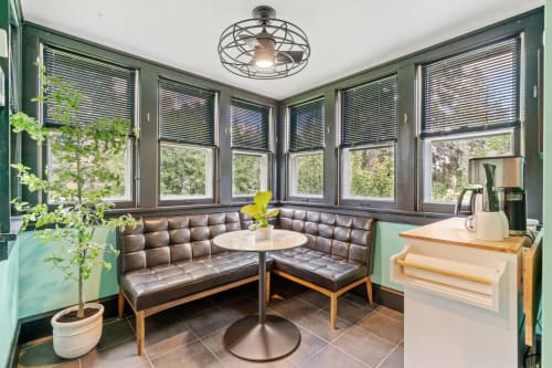 Your bright breakfast nook wraps around corner windows, where leather banquette seating and garden views create the perfect spot for morning coffee.