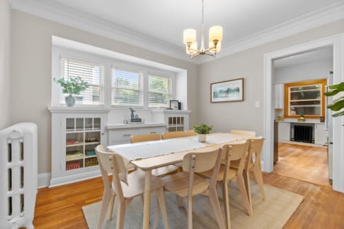 Gather around your elegant dining table with warm wood floors and bright natural light streaming through beautiful windows.