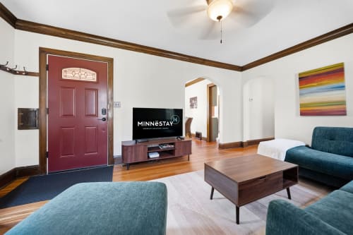 Relax in your spacious living room with warm wood accents, plush teal seating, and vibrant artwork that brightens the space.