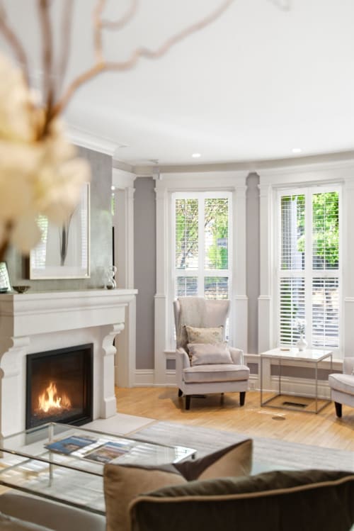 Sink into plush seating by your private fireplace, where tall windows invite soft natural light and garden views into your elegant retreat.